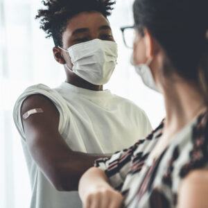 Smiling young people wearing face masks greeting merrily by bumping elbows at workplace . Teenage man and woman in facial covers protected from COVID-19 coronavirus showing friendship and happiness .